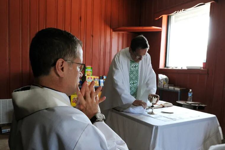 The Rev. William Murphy prepares the Eucharist as the Rev. Joseph Devlin contemplates. (CLEM MURRAY/Staff Photographer)