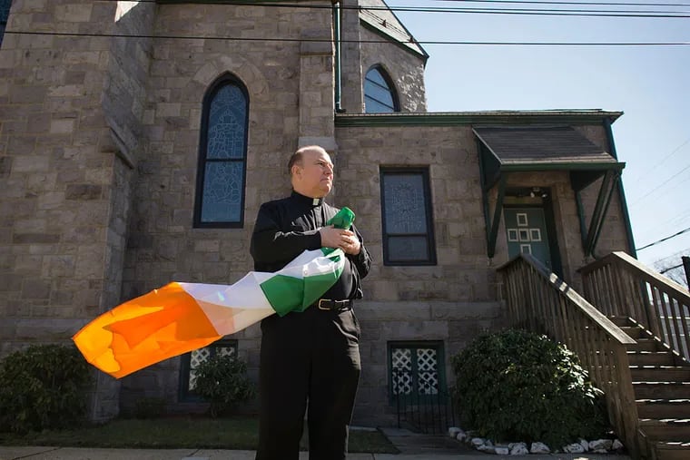 Msgr. William Hodge, who became pastor at St. Mary’s parish in July, holds the flag of Ireland outside his Gloucester City church. “I just couldn’t believe they didn’t have a St. Patrick’s Day parade,“ he said. “I figured the people here would react very positively.”