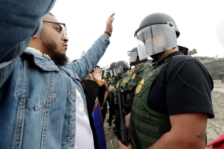 A man holds his hands in the air in front of a line of Border Patrol agents during a protest Monday, Dec. 10, 2018, in San Diego. U.S. officials arrested 32 people at a demonstration Monday that was organized by a Quaker group on the border with Mexico, authorities said. Demonstrators were calling for an end to detaining and deporting immigrants and showing support for migrants in a caravan of Central American asylum seekers. (AP Photo/Gregory Bull)