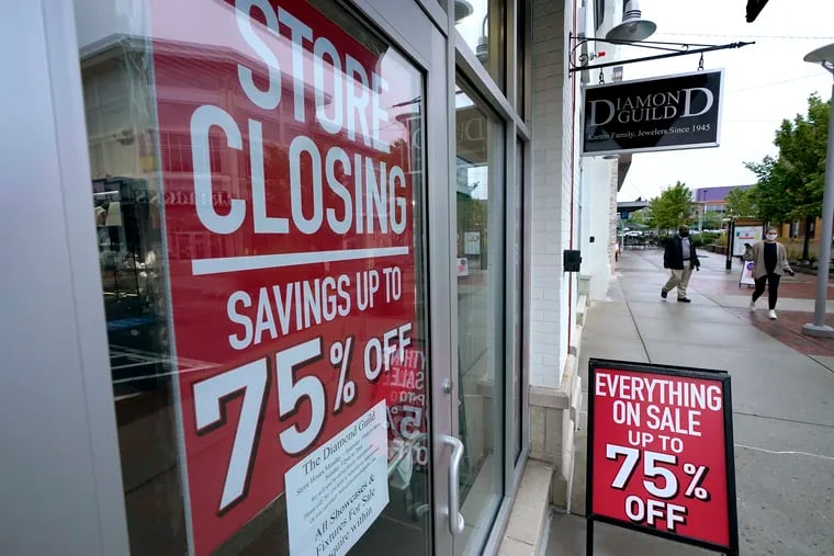 In this Sept. 2 photo, passers-by walk past a business storefront with store closing and sale signs in Dedham, Mass.
