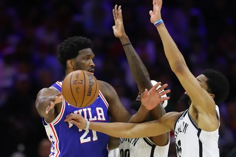 Sixers center Joel Embiid passes the basketball past Brooklyn Nets forward Royce O'Neale and guard Spencer Dinwiddie.