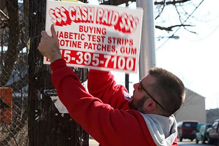 Christopher Sawyer removes a 'bandit' sign at 6th Street and Montgomery Avenue. (Kate McCann / Staff Photographer)