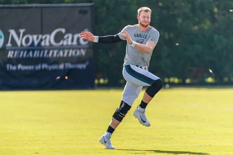 Philadelphia Eagle quarterback Carson Wentz, puts his weight on his left knee as he runs leg crossovers on the field before the beginning of practice during the Eagles training camp at the NovaCare Center on August 2, 2018.