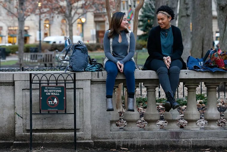 Robin Truitt (left), 19, sits with Dori Markovitz, 18, on the three-foot-high concrete wall lining Rittenhouse Square Park next to a sign banning sitting on the wall on Thursday, Jan. 12.