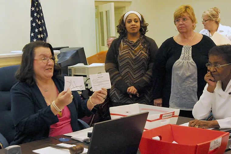 The Atlantic County Board of Elections commissioners reconvene to count provisional ballots in Mays Landing on Nov. 12, 2013.  Here, Chairperson Paula Dunn holds up two signatures to see if they match. ( APRIL SAUL / Staff )