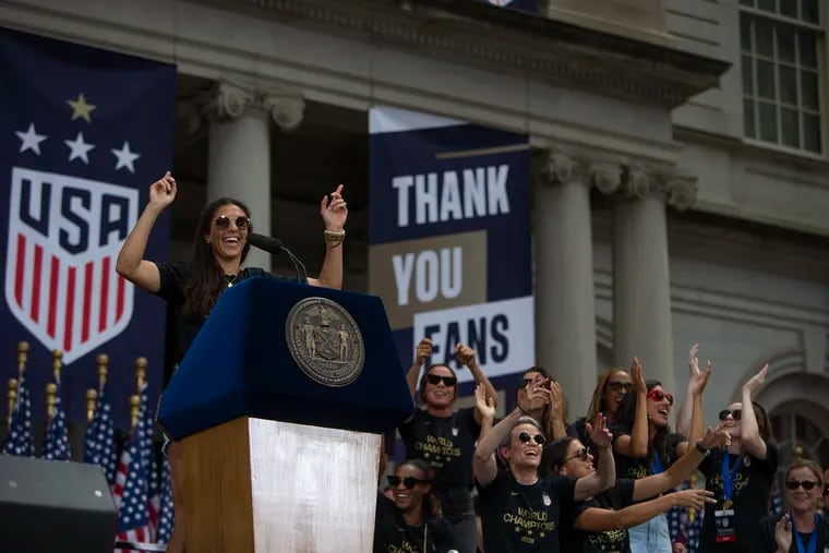 Carli Lloyd speaks to the crowd while her teammates cheer her on outside of New York City Hall at a ceremony following the team's championship parade down the Canyon of Heroes in lower Manhattan for their World Cup win.