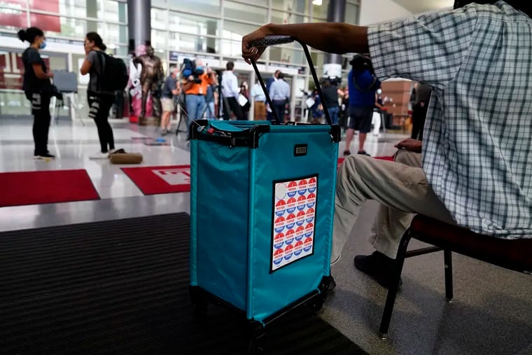 A poll worker hangs on the ballot box at a satellite election office at Temple University’s Liacouras Center, Tuesday, Sept. 29, 2020, in Philadelphia.