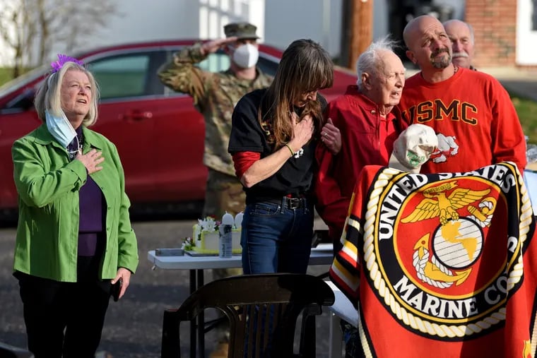 John Welsh (second from right) a U.S. Marine Corps veteran of the Battle of Iwo Jima, and recipient of two Purple Heart medals, sings the national anthem during a drive-by parade for his 100th birthday, outside his Somerdale, N.J. home Dec. 13, 2020. At left is his daughter, Darcy Liberatore, with his grandson Harry Liberatore and family friend Ceal Barton helping him stand.