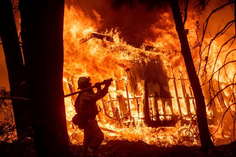 FILE – In this Nov. 9, 2018 file photo, firefighter Jose Corona sprays water as flames from the Camp Fire consume a home in Magalia, Calif. A massive new federal report warns that extreme weather disasters, like California's wildfires and 2018's hurricanes, are worsening in the United States. The White House report quietly issued Friday, Nov. 23 also frequently contradicts President Donald Trump. (AP Photo/Noah Berger, File)