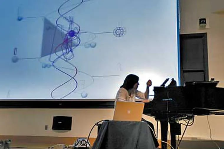 Elaine Chew plays the piano while a computer analyzes her rhythms and splashes graphics on a screen behind her during a concert at Drexel University, part of the 9th International Conference for Music Information Retrieval. (Eric Mencher/Inquirer)