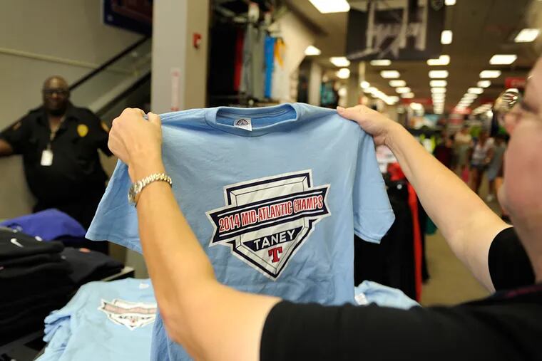 Security guard Anthony Townsend watches as customer Janet Brindley of Havertown sizes Taney t-shirt for purchase at Modell's on Chestnut Street August 19, 2014 as demand is through the roof for Taney Little League gear.