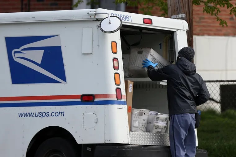 A U.S. Postal Service worker wears gloves while he stops at a collection box on Secane Drive in Northeast Philadelphia in April.