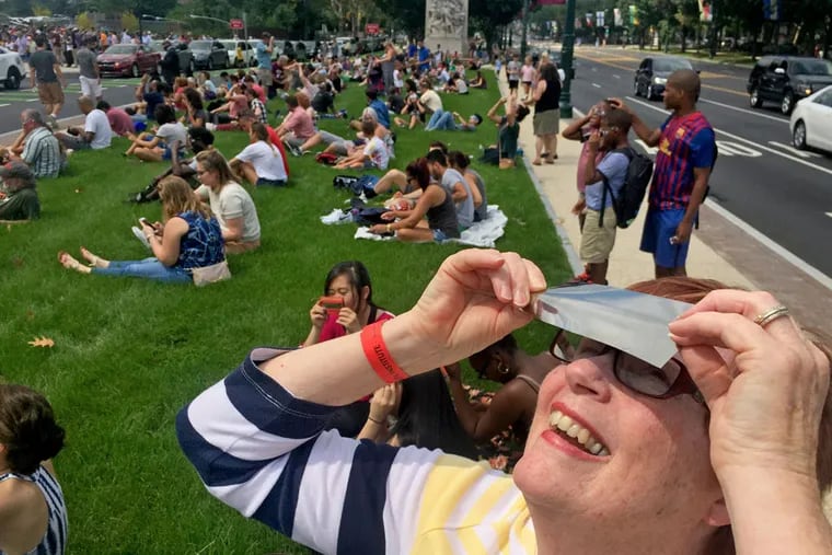 A woman uses a special filter to watch the eclipse with hundreds of others along the Ben Franklin Parkway, outside the Franklin Institute in August 2017. Expect similar scenes Monday.