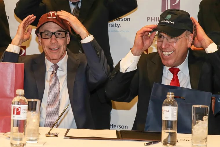 Thomas Jefferson University and Philadelphia University announced a preliminary agreement to merge. At the signing table (from left): Staphen Klasko MD MBA President and CEO, Jefferson, and Stephen Spinelli, Jr., PhD, President, Philadelphia University, trade ball caps after signing the agreement.