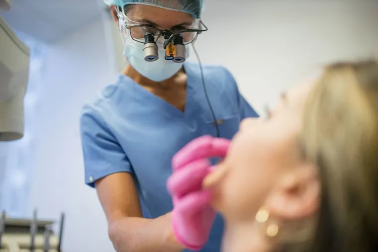 Despina Markogiannakis examines a patient at her dental practice in Chevy Chase, Md. Markogiannakis says she has noticed an increase in patients grinding or clenching their teeth, conditions likely caused by pandemic-related stress.
