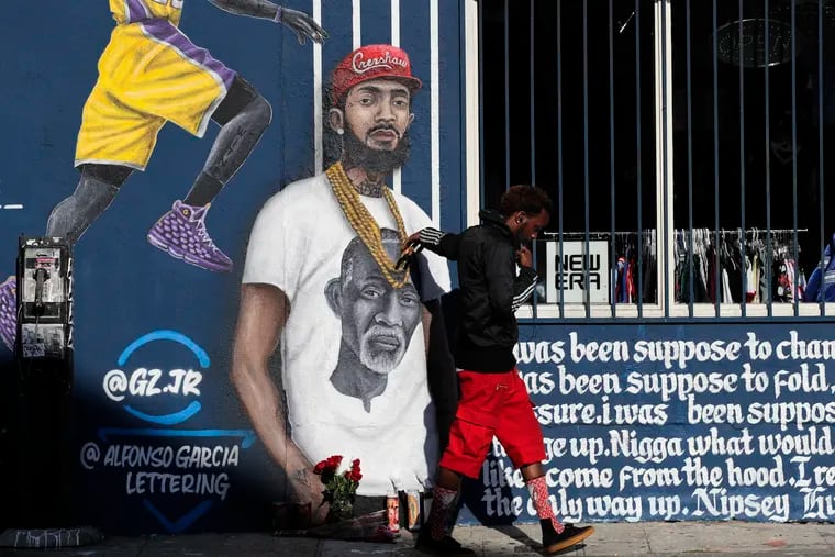 A man touches a mural depicting slain rapper Nipsey Hussle, Tuesday, April 2, 2019, in Los Angeles. Hussle was shot and killed Sunday, March 31, outside of his clothing store in Los Angeles.