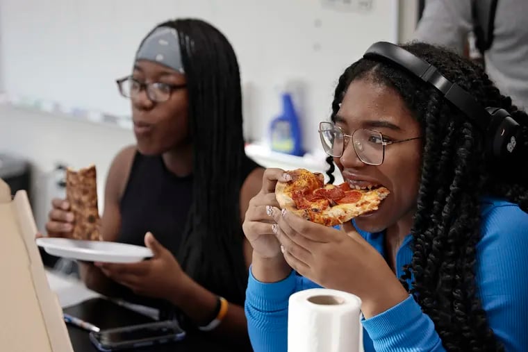 Science Leadership Academy 11th graders Jalop Pewu (left) and Cianney Saunders sample Wawa pizza at the school in Philadelphia.