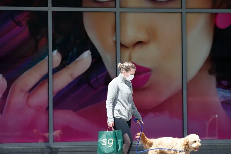 A masked pedestrian walks a dog past an advertisement at the Fashion District Philadelphia, one of PREIT's malls.