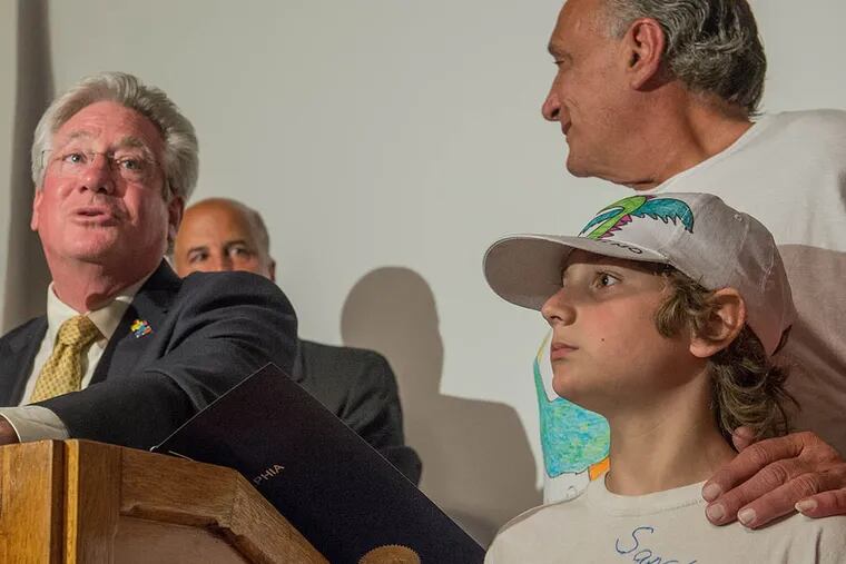 Santino Sagliano (right) stands with his father, Mario, while Councilman Dennis O’Brien presents the boy with a certificate of recognition for his dragon T-shirt designs that raise awareness for autism. (Bryan Woolston/For The Inquirer)