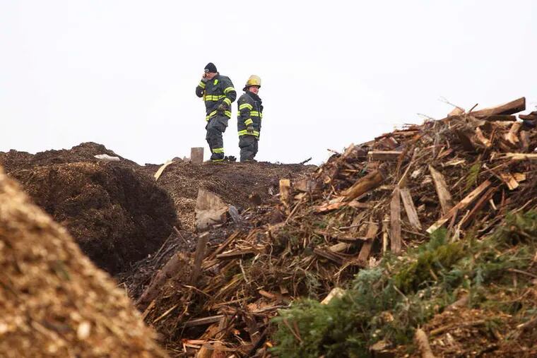 Two city firefighters stand atop a mountain of mulch watching for any lingering hot spots. The fire in the Somerton section raged at its worst Sunday.