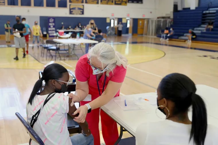 Nurse Kimball Dunlap (center) puts a bandage on the arm of Kimonee Washington, 12, after administering the first dose of the Pfizer COVID-19 vaccine during a vaccination clinic for children 12 and older at Cheltenham High School on May 19, 2021.