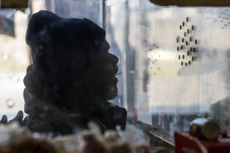 A customer speaks to the holes in the thick barrier glass as he orders a beer in Philly stop-and-go shop.
