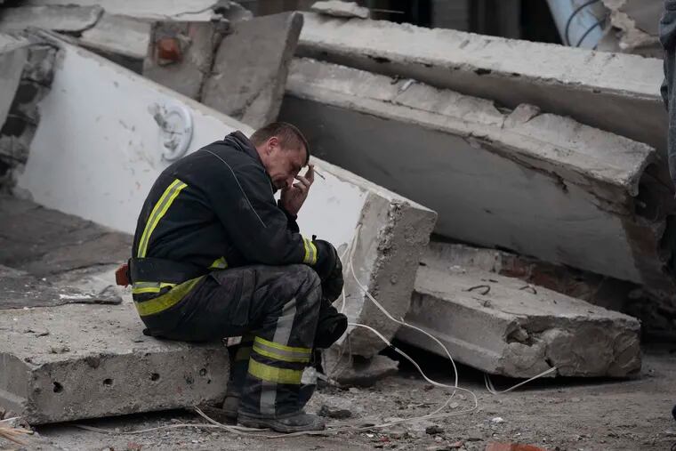 A rescue worker takes a pause as he sits on debris at the scene where a woman was found dead after a Russian attack that heavily damaged a school in Mykolaivka, Ukraine, on Wednesday.