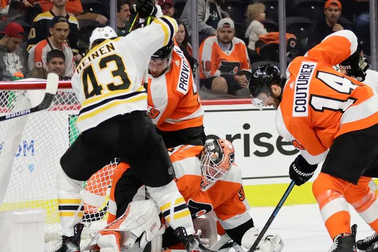 Flyers goalie Brian Elliott goes after the puck with teammates Ivan Provorov and Sean Couturier against Boston winger Danton Heinen during a preseason game last month. Elliott will make his first start of the regular season Tuesday in Calgary.