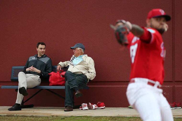 Matt Klentak z9left) and Pat Gillick (right) talk on a bench overlooking the bullpen sessions at spring training.