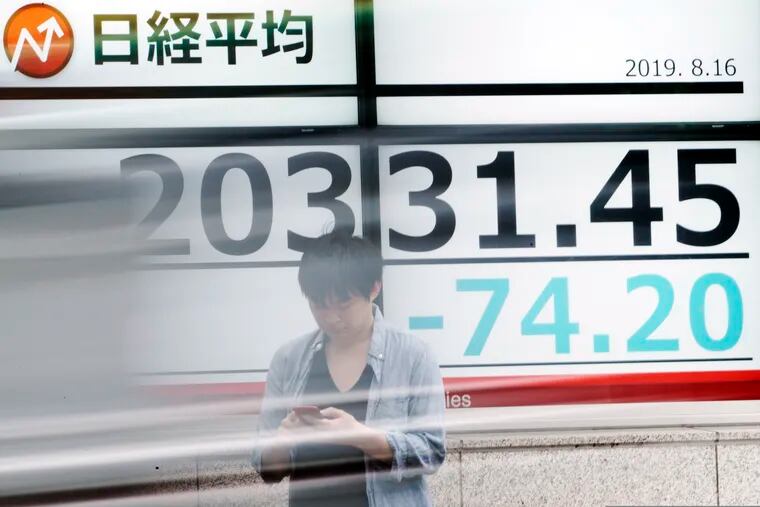 A man stands as a car goes by an electronic stock board showing Japan's Nikkei 225 index at a securities firm in Tokyo Friday, Aug. 16, 2019. Asian shares were mixed Friday as turbulence continued on global markets amid ongoing worries about U.S.-China trade conflict.
