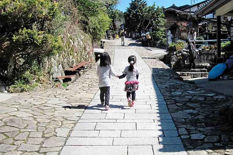 Two girls walk a stone-paved main street of one of the small villages along the Nakasendo Way. Nakasendo reached the peak of its usefulness and romance during Japan's Edo Period (1603-1868); since the highway linked two of the biggest cities, speeding commerce and messages, it was at the heart of that golden age. (Peter Mandel/Washington Post)