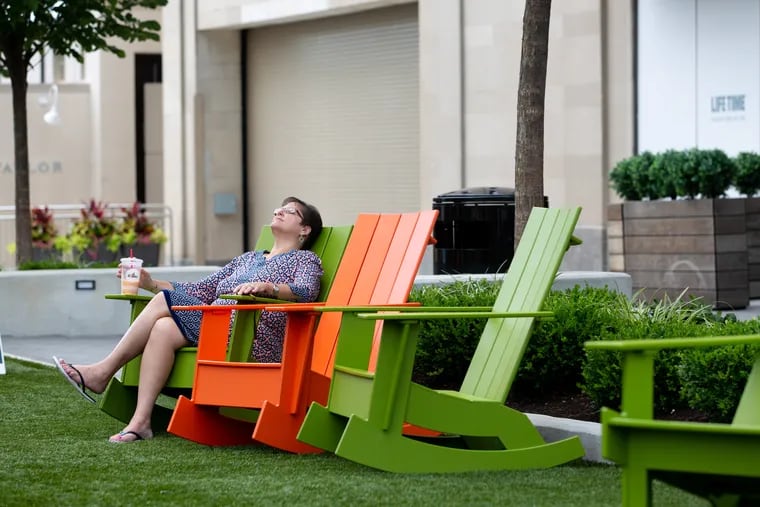 Linda Messina, who works in the Times Building at Suburban Square, rests on the new turf lawn during her lunch break in Ardmore, Wednesday July 31, 2019. Construction work continues to upend what is known as America's oldest shopping center.