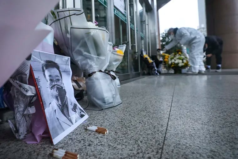 People pay condolence in front of flowers lying near a photo of the late Dr. Li Wenliang at a hospital in Wuhan in central China's Hubei province, Friday, Feb. 7, 2020. The death of the doctor who was reprimanded for warning about China's new virus triggered an outpouring Friday of praise for him and fury that communist authorities put politics above public safety. In death, Dr. Li Wenliang became the face of simmering anger at the ruling Communist Party's controls over information and complaints that officials lie about or hide disease outbreaks, chemical spills, dangerous consumer products or financial frauds.