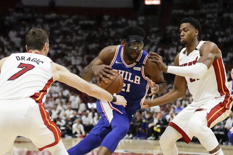 Sixers center Joel Embiid drives to the basket against Miami Heat center Hassan Whiteside (right) and guard Goran Dragic in game three of the Eastern Conference quarterfinals on Thursday, April 19, 2018 in Miami.
