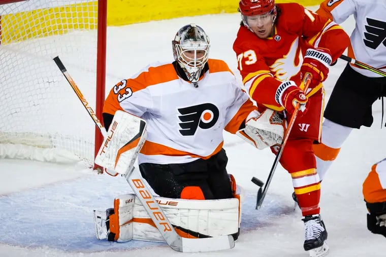 Philadelphia Flyers goalie Samuel Ersson, left, looks on as Calgary Flames forward Tyler Toffoli tries to deflect the puck into the net during the first period of an NHL hockey game in Calgary, Alberta, Monday, Feb. 20, 2023. (Jeff McIntosh/The Canadian Press via AP)