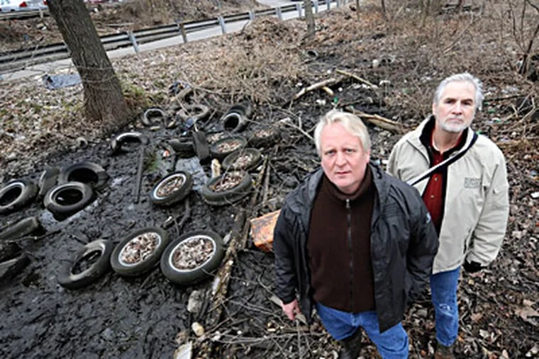 GOAL president Dale Frazier (left) and board member Ed Armstrong stand next to discarded tires at a Levittown site. Frazier estimates that the organization has removed 35 tons of debris, 700 tires. (Clem Murray / Staff Photographer)