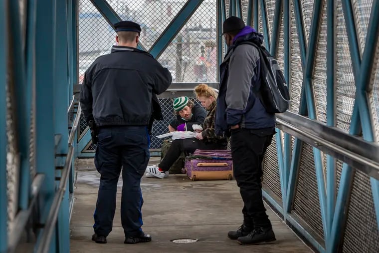 SEPTA Transit Officer Alexander Bires and outreach specialist Kenneth Harris (right) approach a woman interested in getting help with her addiction at the Somerset Station of the Market Frankford El. She is eating breakfast while sitting on her suitcase.