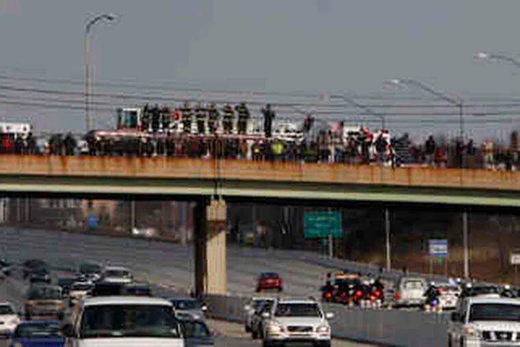 On an I-95 overpass, firefighters salute and citizens pay respect to Philadelphia Officer John Pawlowski as his funeral procession heads to Resurrection Cemetery in Bensalem.