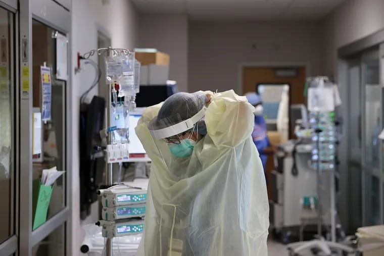A medical worker puts on personal protective equipment before entering a patient room inside a COVID-19 intensive care unit at Temple University Hospital's Boyer Pavilion in North Philadelphia on Tuesday, April 7, 2020. Health workers nationwide, strapped for protective equipment, have had to scramble for solutions going by unclear guidelines from officials.