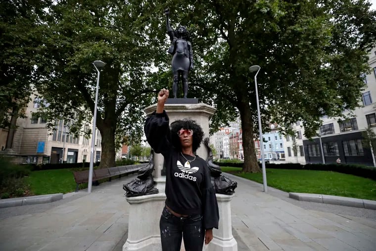 Jen Reid poses for photographs in front of the new black resin and steel statue portraying her, entitled "A Surge of Power (Jen Reid) 2020" by artist Marc Quinn after the statue was put up this morning on the empty plinth of the toppled statue of 17th century slave trader Edward Colston, which was pulled down during a Black Lives Matter protest in Bristol, England, Wednesday, July 15, 2020. On June 7 anti-racism demonstrators pulled the 18-foot (5.5 meter) bronze likeness of Colston down, dragged it to the nearby harbor and dumped it in the River Avon — sparking both delight and dismay in Britain and beyond.