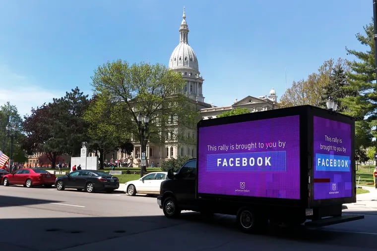 A video sign about Facebook is shown on a truck at the State Capitol during a rally in Lansing, Mich., Wednesday, May 20, 2020. Barbers and hair stylists are protesting the state's stay-at-home orders, a defiant demonstration that reflects how salons have become a symbol for small businesses that are eager to reopen two months after the COVID-19 pandemic began. (AP Photo/Paul Sancya)