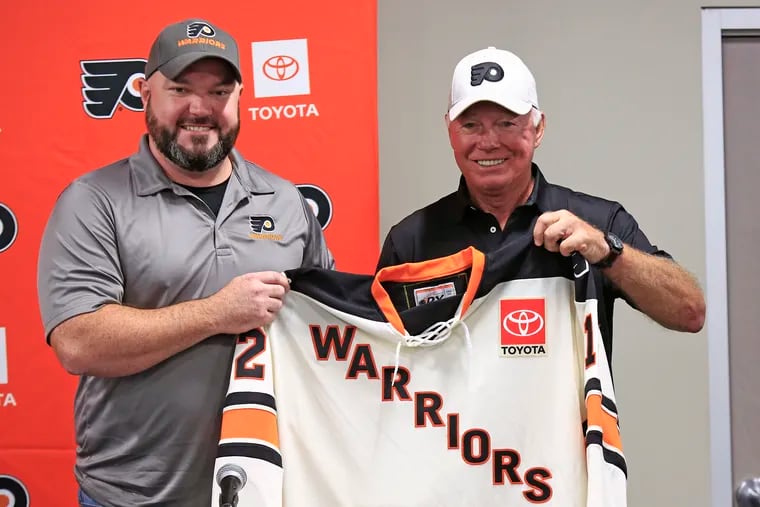 Flyers senior adviser Bob Clarke (right) presents a Philadelphia Flyers Warriors jersey to Jim Young, captain of the Warriors, a team of disabled and injured military veterans, during a press conference at training camp Saturday in Voorhees.