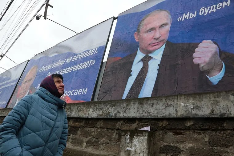 A woman walks past placards bearing images of Russian President Vladimir Putin reading "Russia does not start wars, it ends them" (left) and "We will aim for the demilitarization and denazification of Ukraine" in Simferopol, Crimea, earlier this month.