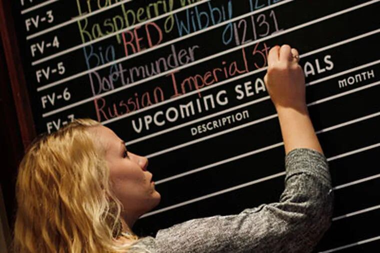 Samantha Park writes the day's beer offerings on a chalk board at the new Chestnut Hill branch of Iron Hill Brewery .