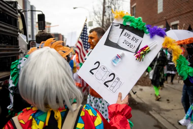 A mummer holds a sign saying “Bye Bye 2020,” with sanitizer stuck on it and drawings of toilet paper rolls, during a march along 2 Street on New Years Day on Friday, Jan. 1, 2021. Despite orders from the city a few hundred mummers hold a small march.