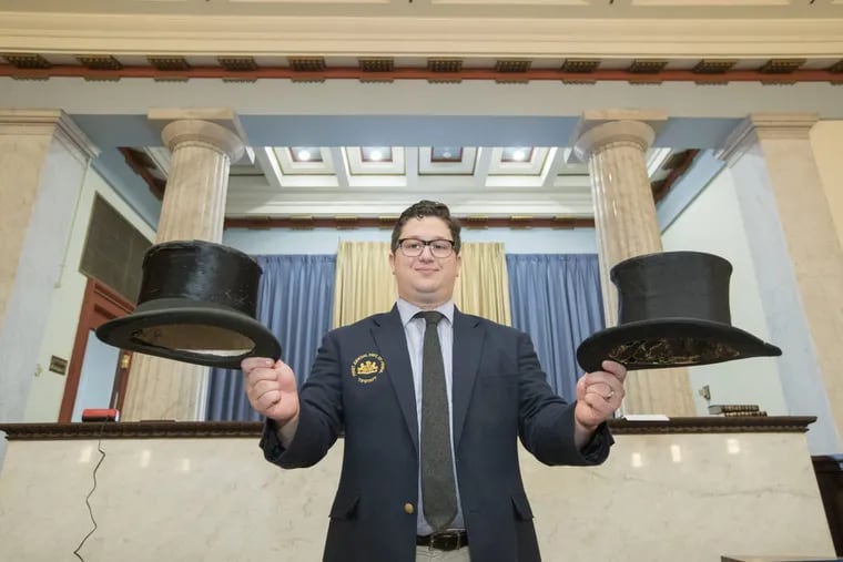 Common Pleas law clerk Matthew Richards holds two battered top hats, one of which will be used to collect ballots from the 88-member Board of Judges, which will vote Thursday for an interim district attorney in Philadelphia.