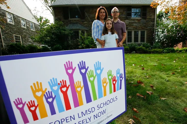 Parents Anna and Eric Mauro with their daughter Juliette and a "Reopen Lower Merion School District Schools" lawn sign at their Merion Station home. Juliette Mauro is a fourth-grader and is struggling with her computer-based school days.