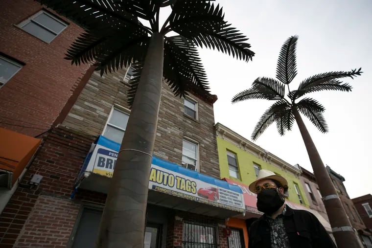 Artist Raúl Romero explores how Puerto Ricans in Philly connect to the island through sound, specifically through the singing of the iconic frog, in his latest exhibit at Taller Puertorriqueño. In the photo, Romero walks pass iron palm trees on 5th Street and Lehigh Avenue, that are part of his exhibit in the Fairhill neighborhood of Philadelphia.