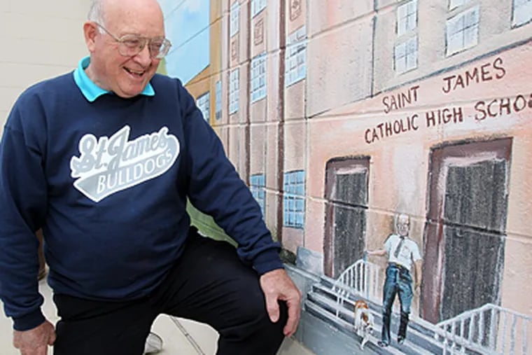 Former assistant principal John Mooney, Class of 1950, kneels by a mural of St. James Catholic High in Chester that shows him leaving with Boomer the bulldog. (Charles Fox / Staff Photographer)