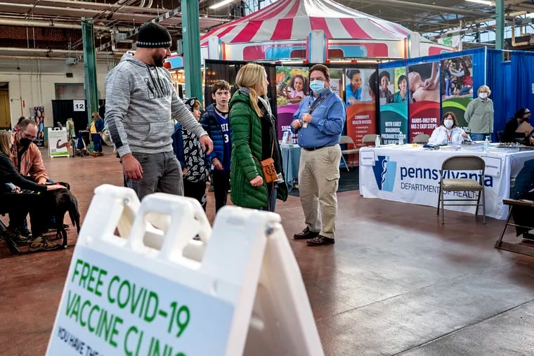 Tom McGroaty (center, wearing mask) with the Pennsylvania Department of Health, works like a carnival pitchman or barker, trying to attract attendees to the department’s COVID-19 vaccine pop-up clinic at the Pennsylvania Farm Show Jan. 10, 2022. The show returned to Harrisburg for its 106th year, after being virtual last year,
